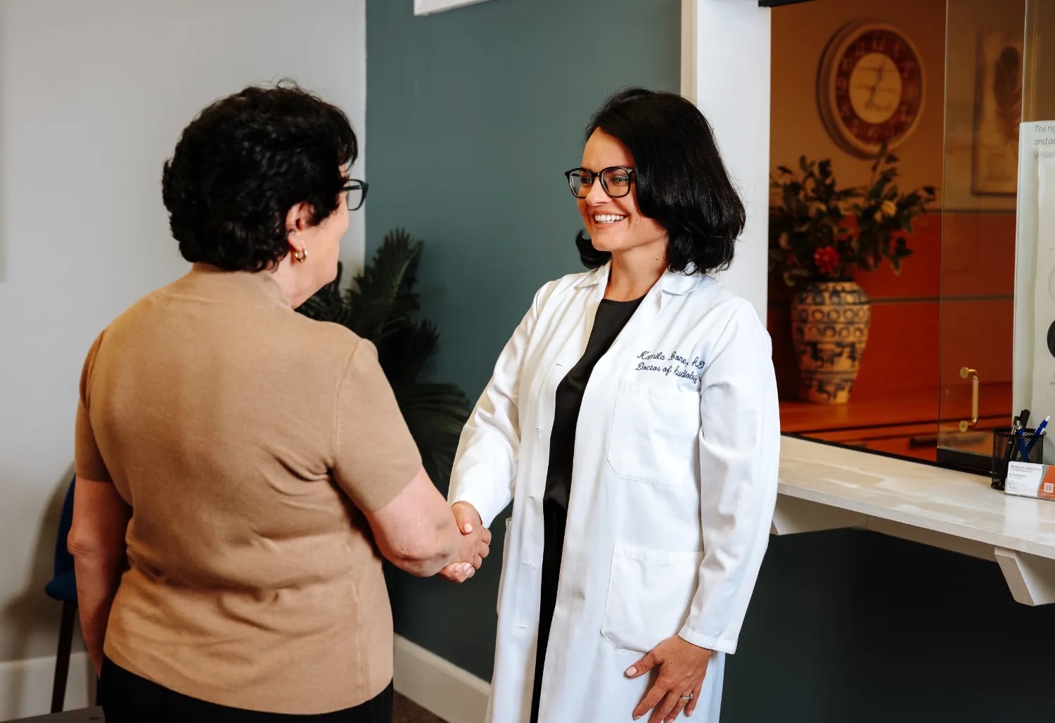 Dr. Bome in her white coat, smiling as she shakes hands with a patient at the front desk